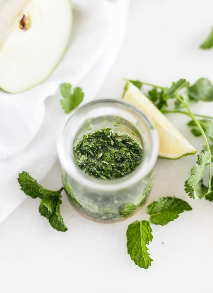 cilantro mint vinaigrette in a small glass container surrounded by lime and apple wedges and herbs.