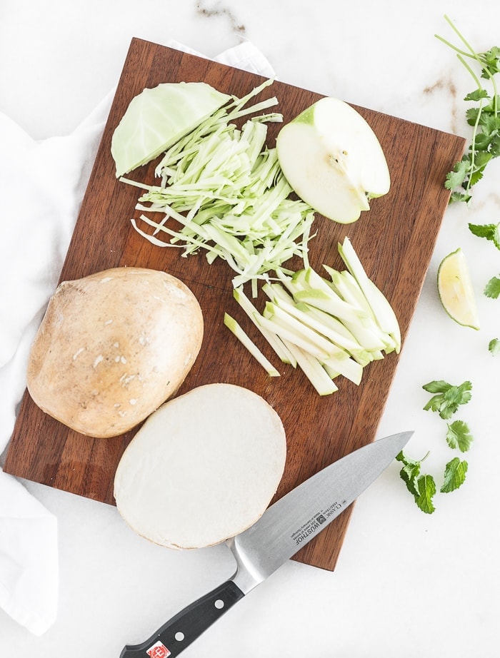 overhead shot of jicama slaw ingredients on a brown cutting board with a chefs knife.