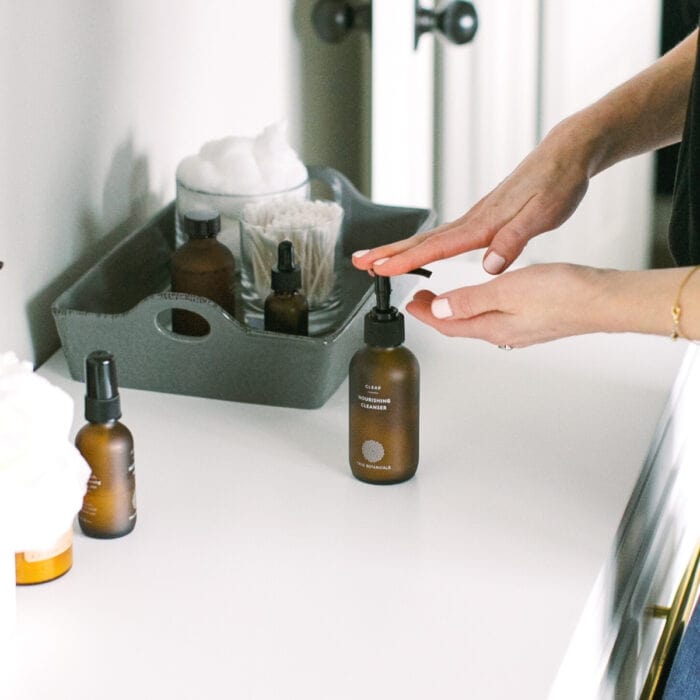 hands pumping face wash from a brown bottle on a white counter.
