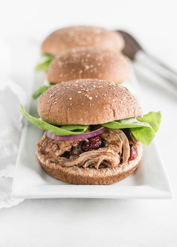 cranberry chipotle pulled pork sandwiches on bun with lettuce lined up on a white platter.