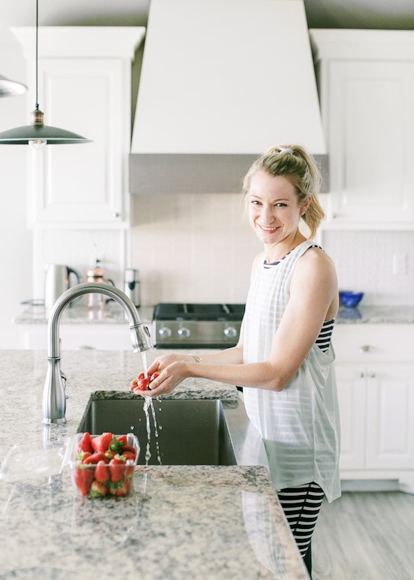 Woman in a blue tank top washing strawberries at the kitchen sink.