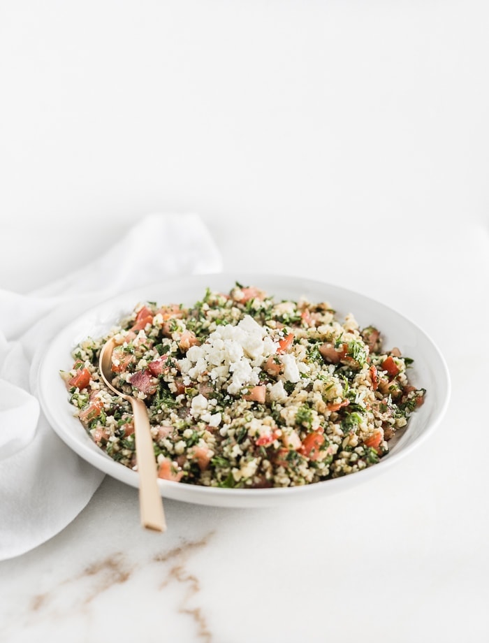 carrot top tabbouleh in a white bowl with feta on top and a gold spoon in the bowl.