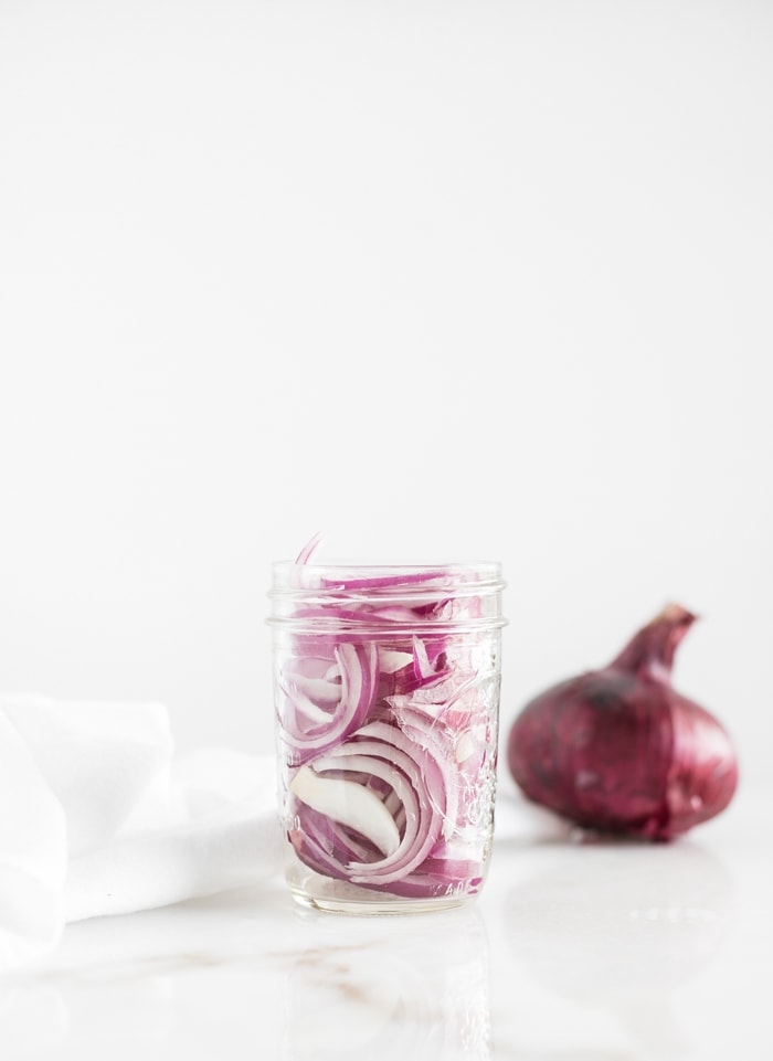 jar of sliced red onions with a whole onion in the background.