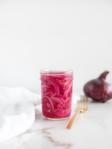 pickled red onions in a jar with a gold fork next to it and an onion in the background.