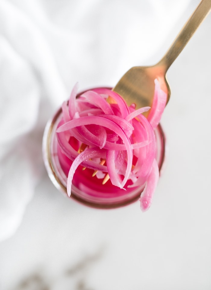overhead shot of a fork lifting pickled red onions from a jar.