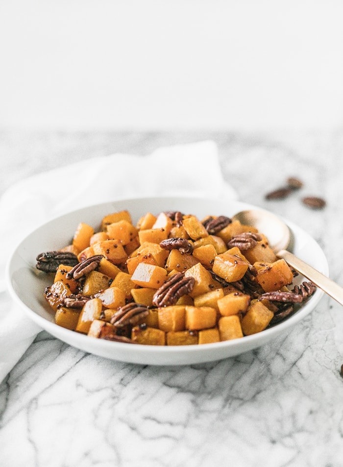 roasted butternut squash cubes with pecans in a white bowl with a gold spoon.