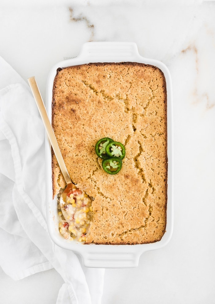 overhead view of southwest creamed corn casserole in a white rectangular baking dish with a gold spoon in the corner where some has been scooped out.