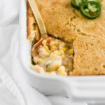 southwest creamed corn casserole with cornbread topping in a white rectangular baking dish with a gold spoon in it.