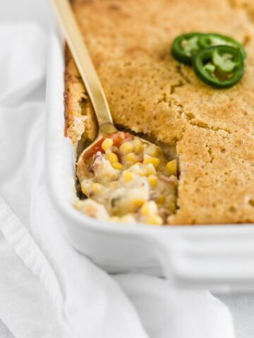 southwest creamed corn casserole with cornbread topping in a white rectangular baking dish with a gold spoon in it.