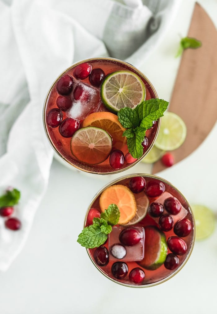 overhead view of two glasses of christmas punch with cranberries, sliced citrus and mint leaves