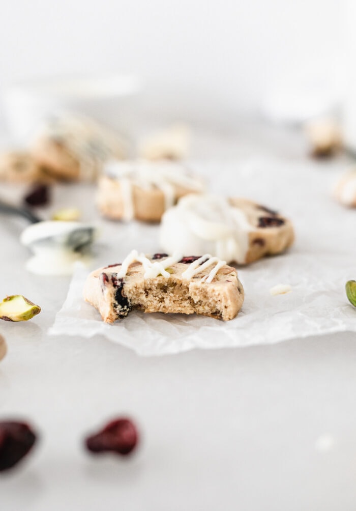 cranberry pistachio shortbread cookie drizzled with white chocolate with a bite taken out of it.