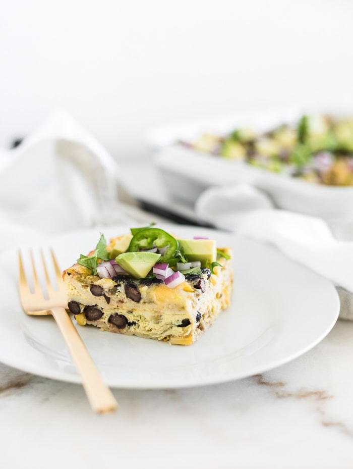 square of Mexican breakfast casserole on a white plate with a gold fork.