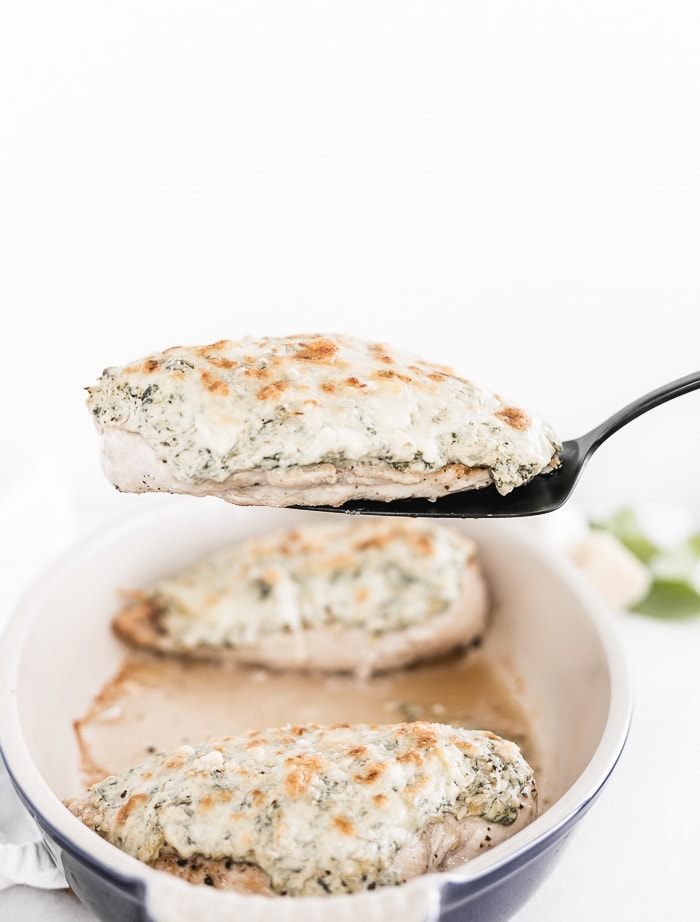 black serving fork lifting a spinach artichoke chicken breast from an oval baking dish.