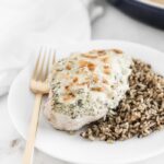 baked spinach artichoke chicken breast on a white plate with rice and a gold fork.