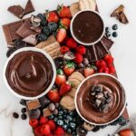 overhead view of berries, chocolates, and chocolate spreads on a brown wooden board.