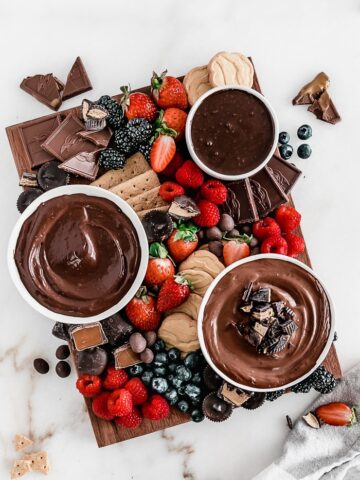 overhead view of berries, chocolates, and chocolate spreads on a brown wooden board.