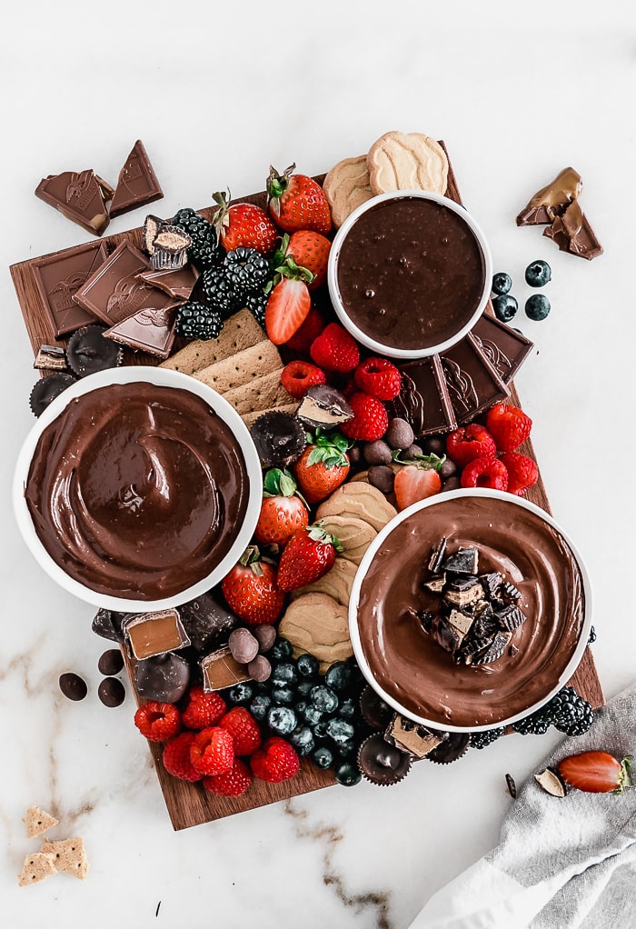 overhead view of berries, chocolates, and chocolate spreads on a brown wooden board.