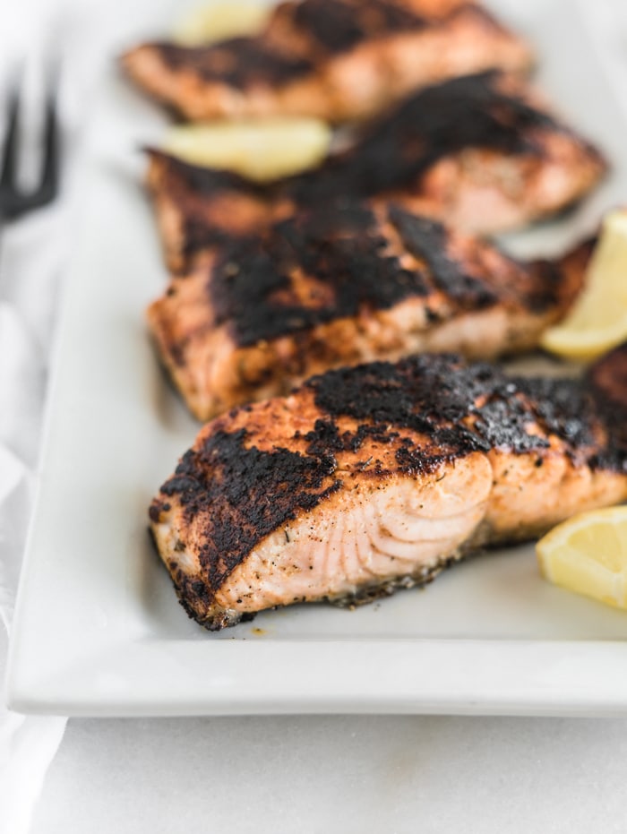 blackened salmon filets on a white rectangular platter with lemon wedges.