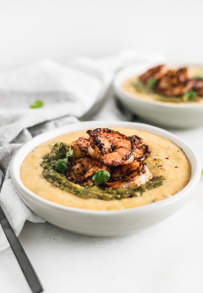 blackened shrimp and green chile puree on top of green chile cheddar grits in a white bowl.