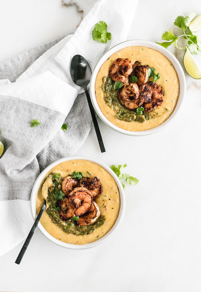overhead image of two bowls of green chile cheddar grits topped with blackened shrimp with two black spoons.