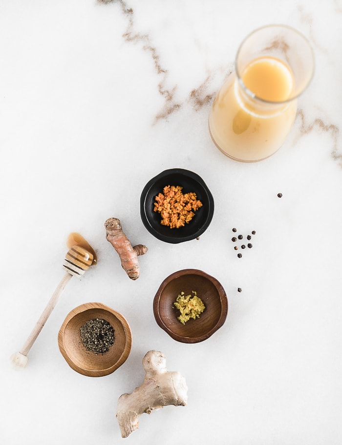 overhead shot of ingredients for honey turmeric ginger shot on a white marble backdrop.