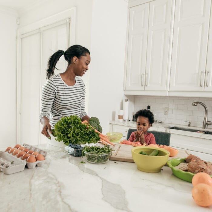woman and toddler in the kitchen with various food on the counter.