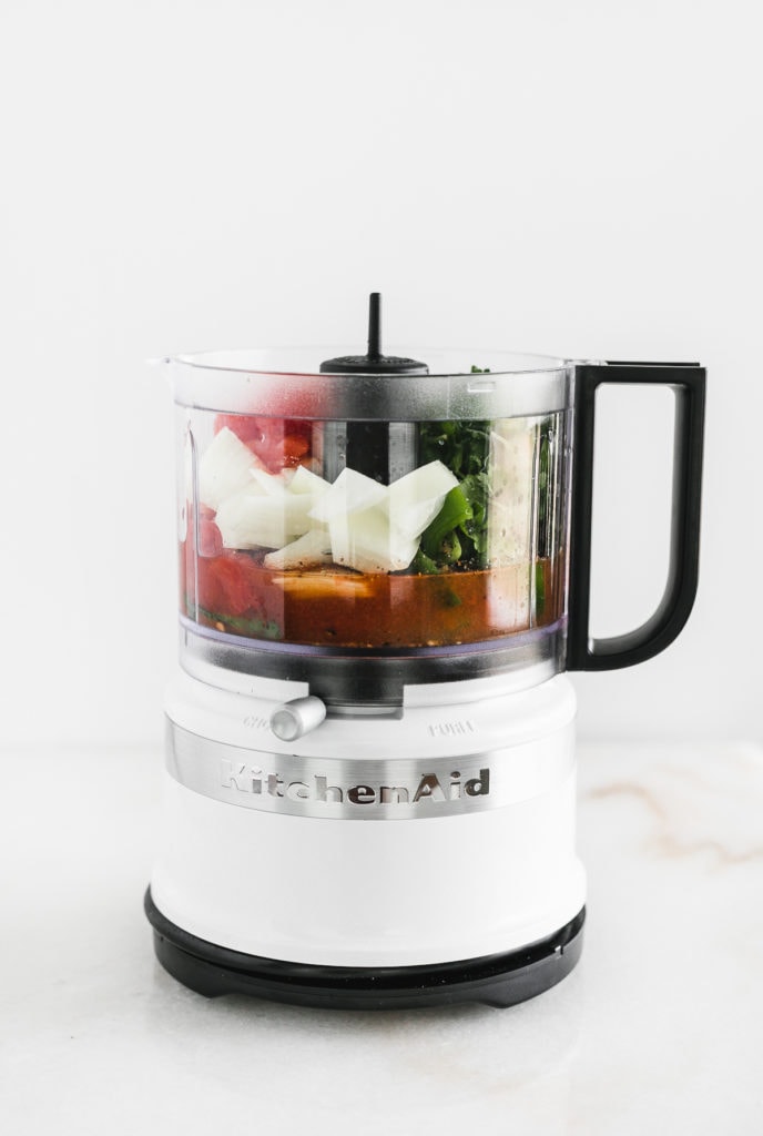 white kitcheniad mini food processor with salsa ingredients in it.