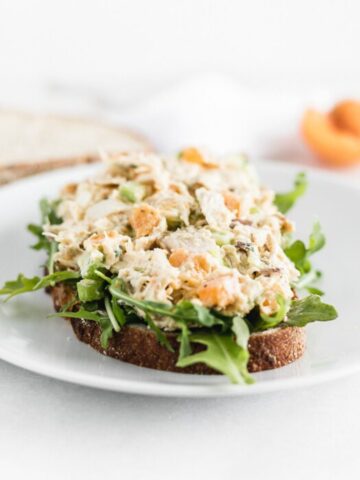 apricot chicken salad on top of arugula on a slice of bread.