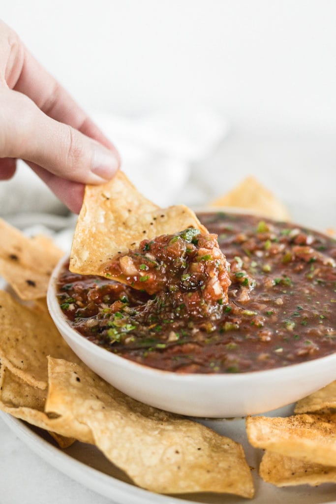 hand dipping a tortilla chip into a bowl of homemade salsa.