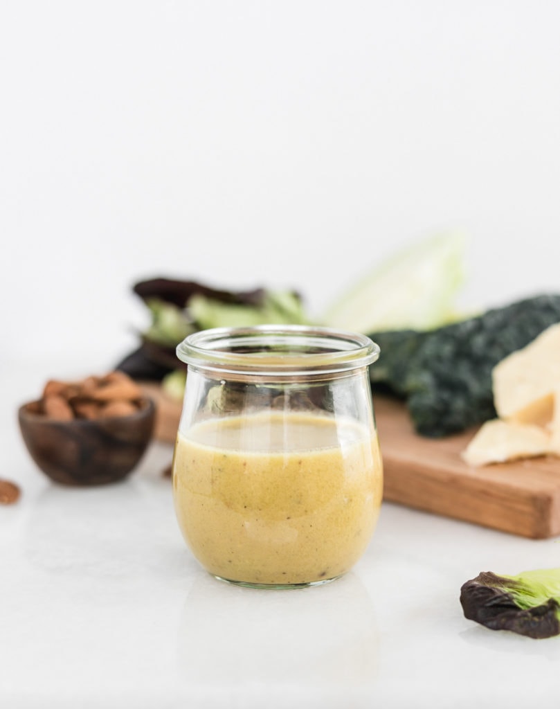 jar of honey mustard bacon dressing with salad ingredients in the background.
