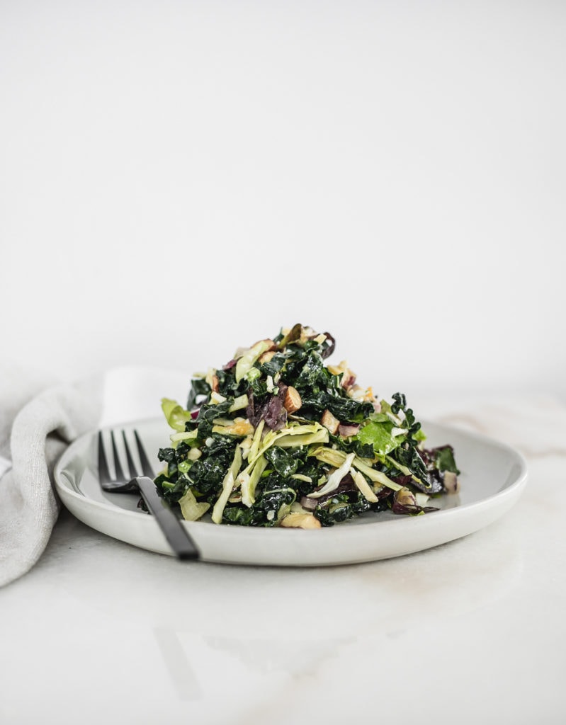 kale salad piled on top of a white plate with a black fork.
