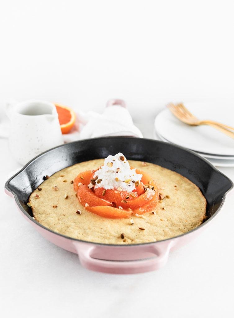 pink cast iron skillet with a baked pancake, topped with cara cara oranges and cardamom whipped cream. 