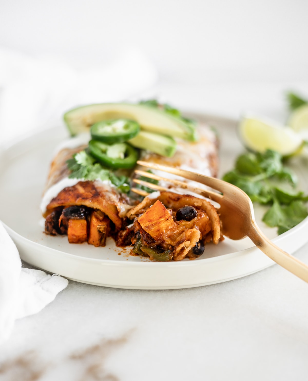 gold fork cutting off a piece of sweet potato black bean enchilada.