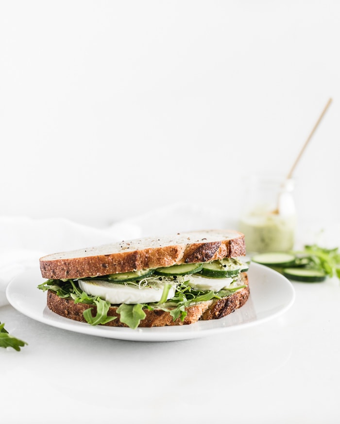 green goddess sandwich on a white plate with a jar of green goddess dressing in the background.