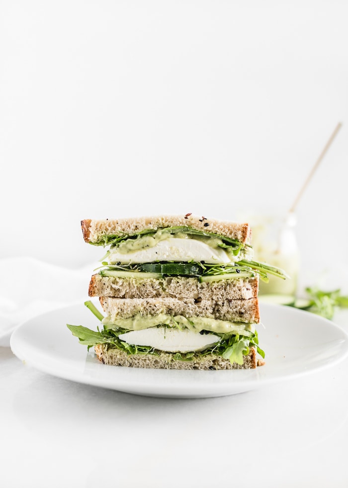 green goddess sandwich with mozzarella cut in half and stacked on a white plate.