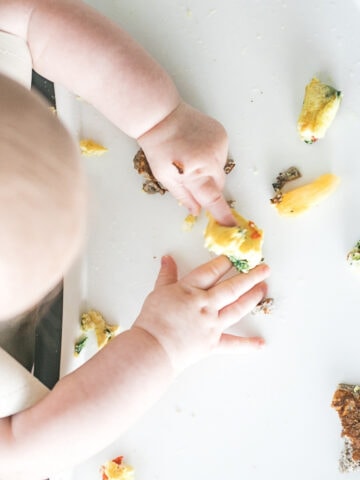 overhead view of a baby's hands on a tray with pieces of food.