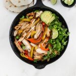 overhead view of chicken fajitas with peppers and onions in a skillet.