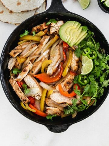 overhead view of chicken fajitas with peppers and onions in a skillet.