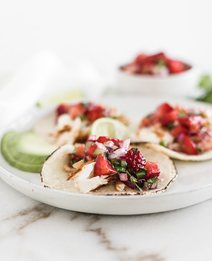 Grilled fish tacos with strawberry salsa on a white plate with avocado slices.