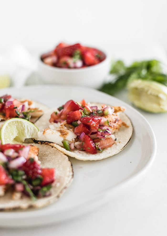 Grilled fish tacos with strawberry salsa on a white plate.