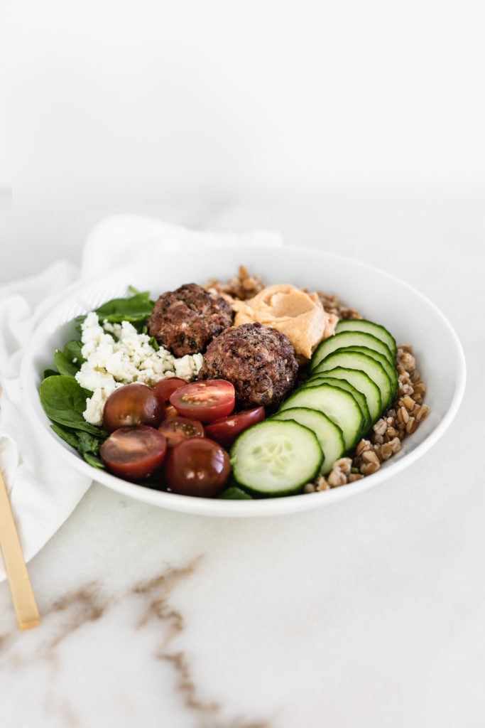 mediterranean grain bowl with meatballs in a white bowl on a white background.