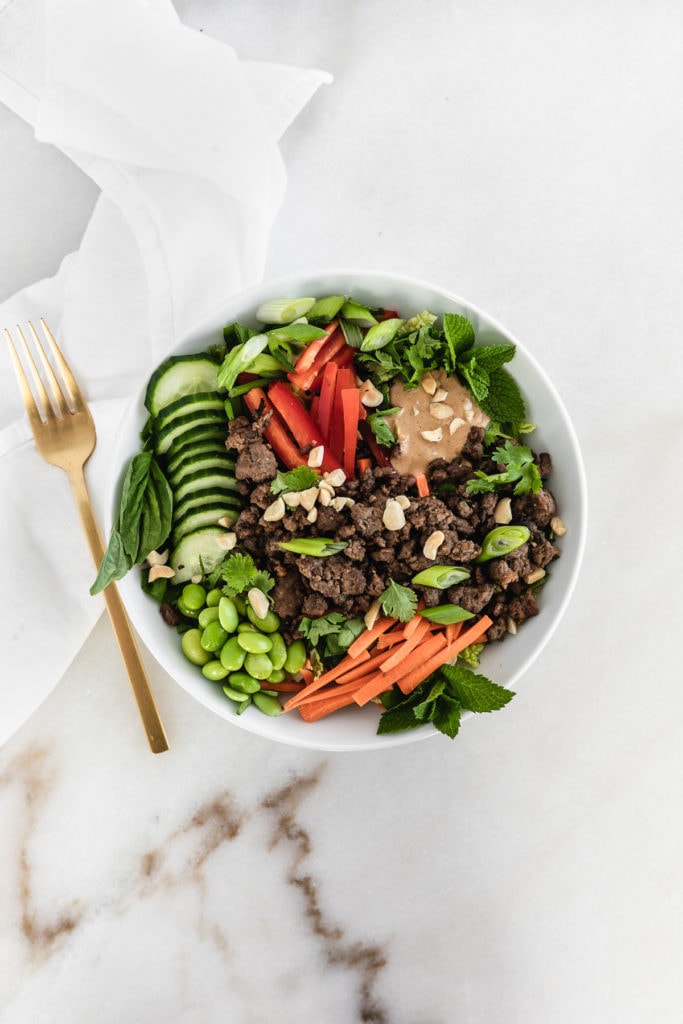 asian inspired salad with ground beef in a bowl with a gold fork beside it.