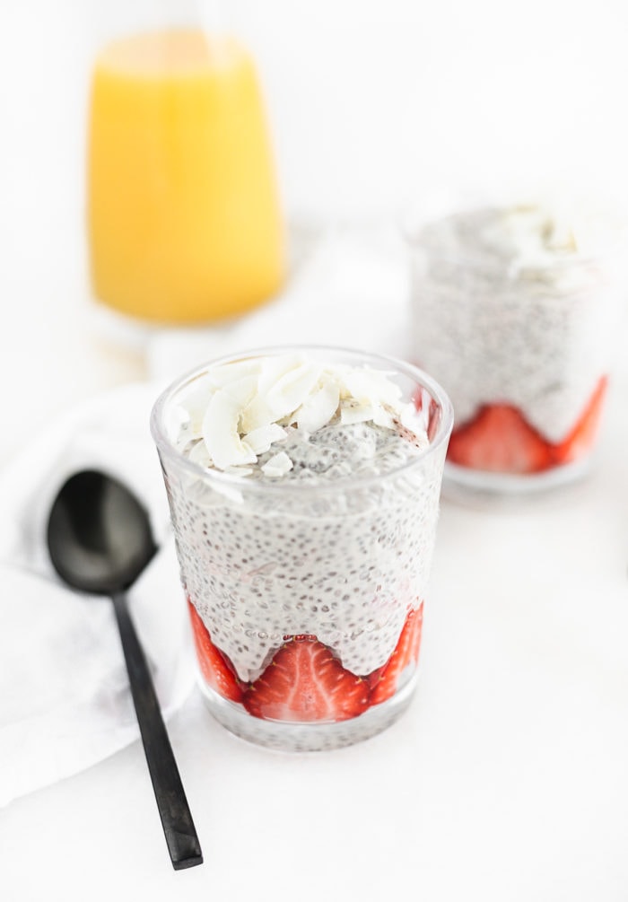 cup of strawberry orange chia pudding with a black spoon beside it and coconut on top.