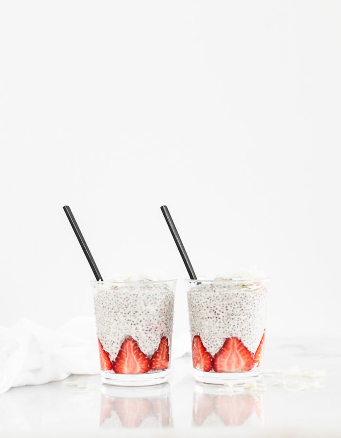 two glasses of strawberry orange chia pudding with black spoons in them.