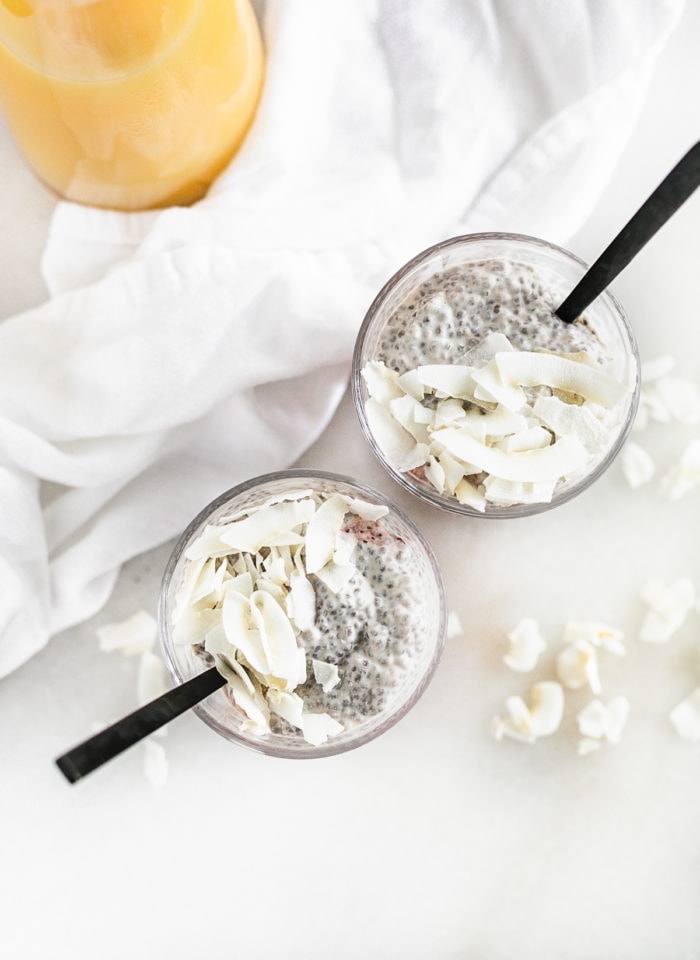 overhead view of two cups of orange juice chia pudding with coconut on top and black spoons in them.