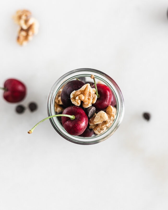 overhead view of cherries, walnuts and chocolate chips in a glass jar.