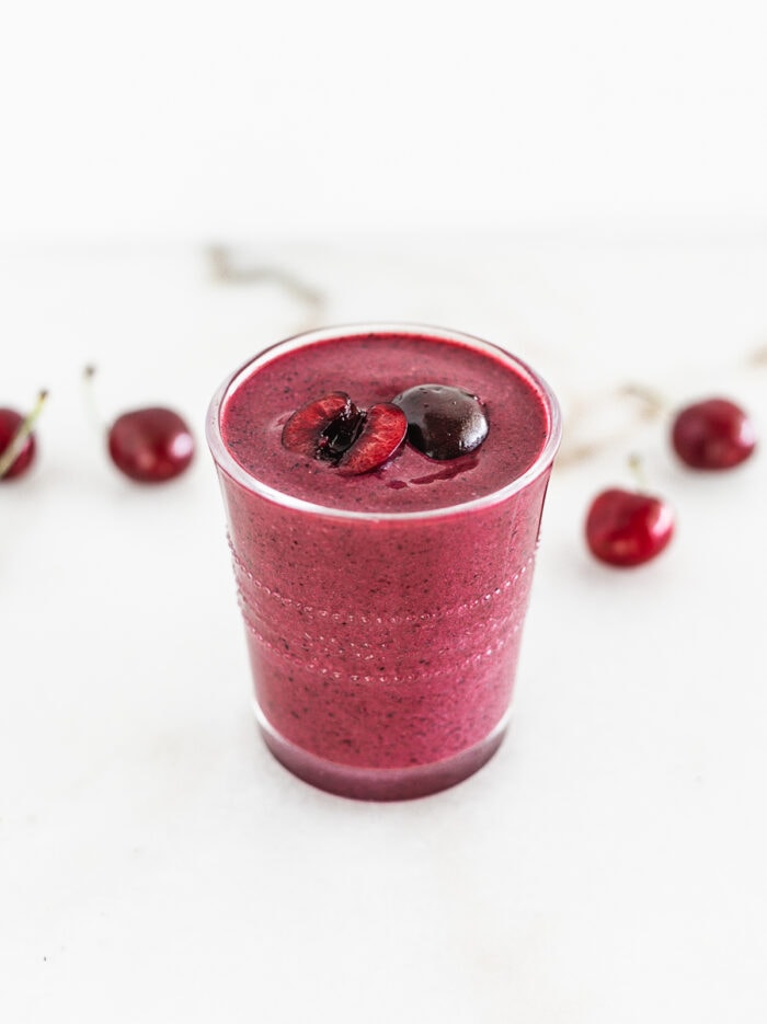 cherry berry probiotic smoothie in a glass with cherries on top and behind it.