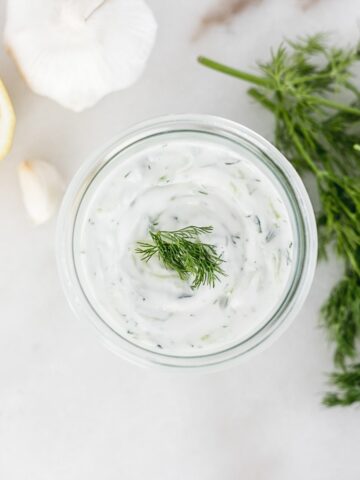 overhead view of homemade tzatziki sauce surrounded by dill, lemon and garlic.
