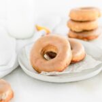two peach donuts with brown sugar glaze on a plate with a stack of donuts in the background.