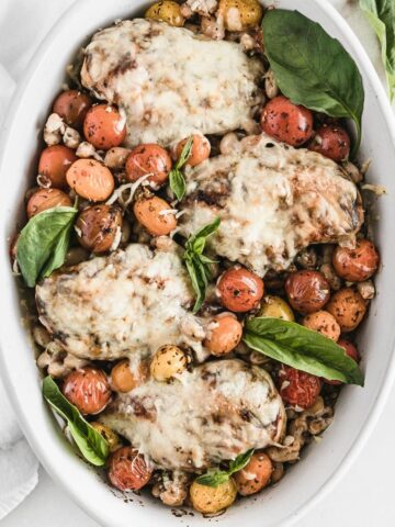 overhead view of white oval baking dish with mozzarella covered chicken, tomatoes, and basil on top of farro.